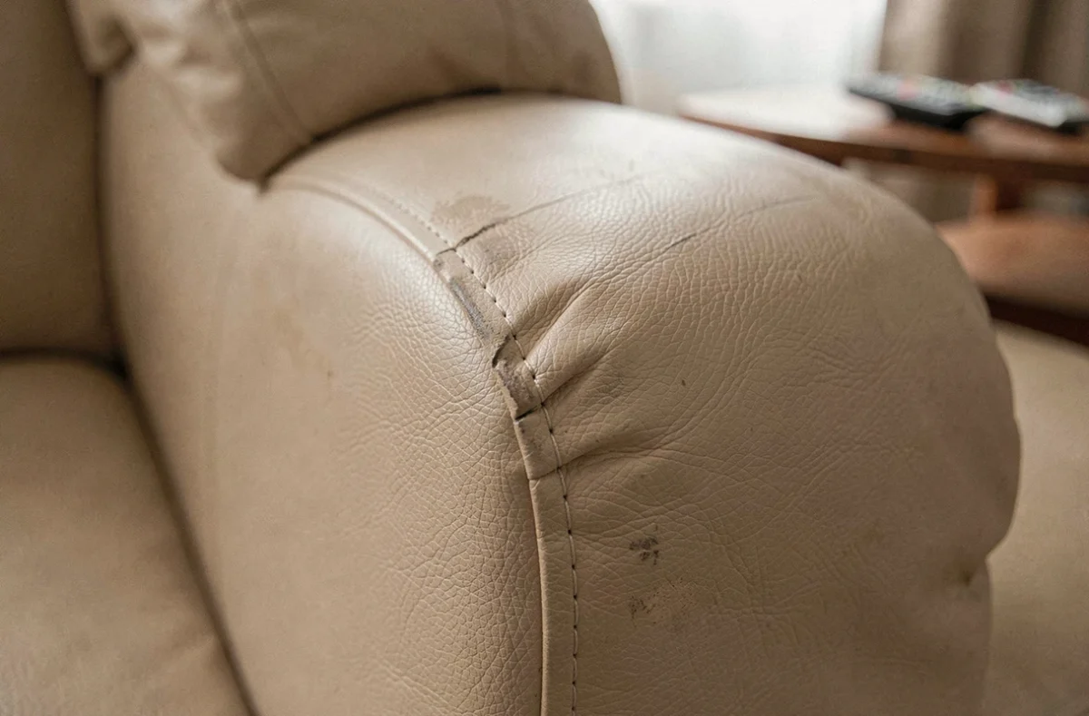 Gros plan sur l'accoudoir et les coutures d'un canapé Poltronesofa en similicuir beige montrant les signes d'usure après deux ans d'usage quotidien
